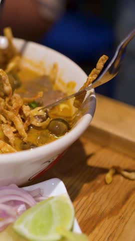 Close-up shot of a spoon lifting yellow curry soup from a bowl of Khao Soi