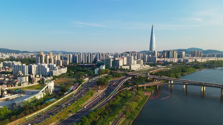 Panoramic aerial siways of iconic Lotte World Tower skyscraper rising over Han River, traffic on Olympic-daero expressway and Olympic bridge under clear blue sky in Seoul South Korea