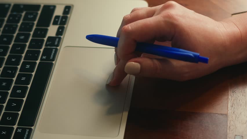 Close-up of female hand holding a pen while working on a laptop. Business planning, online work, studying and productivity concept. High quality 4k footage