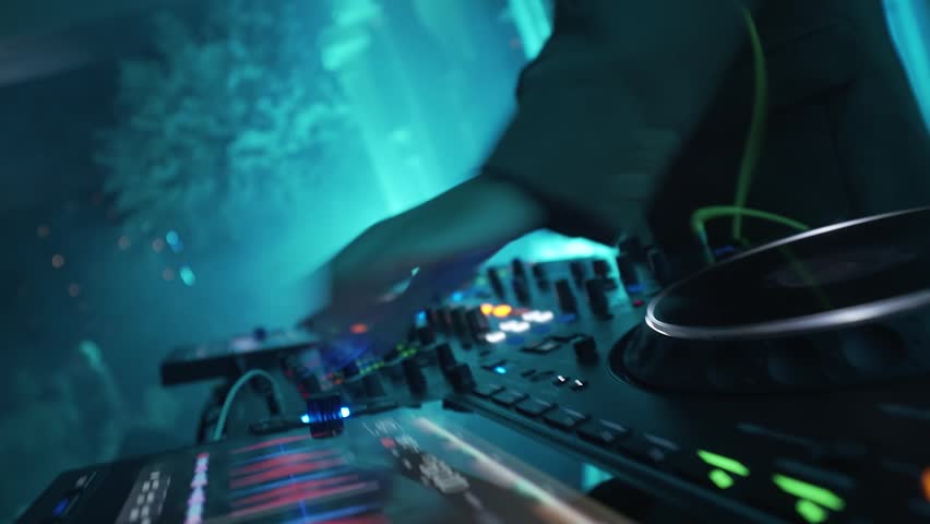 A DJ is playing the DJ equipment on stage, arranging the music with focus and style.