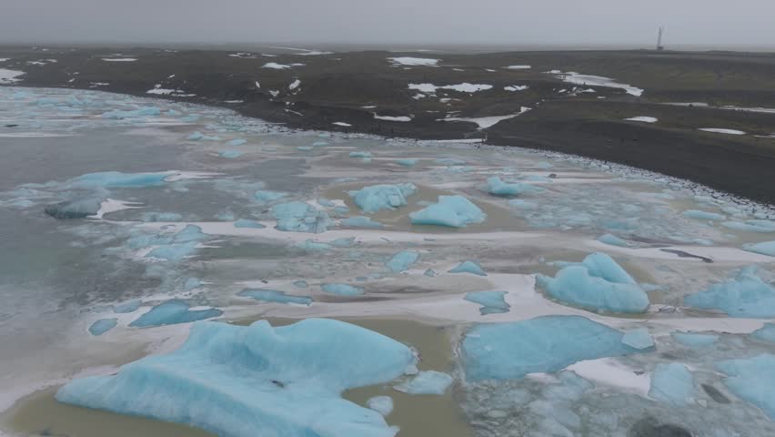 Aerial view of Fjallsarlon glacier lagoon with blue icebergs floating in the water and dark volcanic shores in Fjallsarlon, Sveitarfelagid Hornafjordur, Iceland.