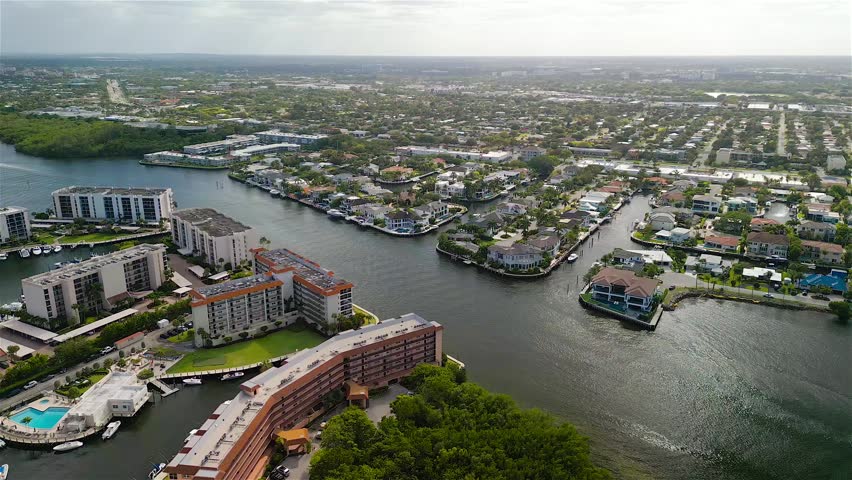 Aerial view of luxury waterfront homes and residential canals surrounded by lush greenery and apartment buildings in Boca Raton, Florida, United States.