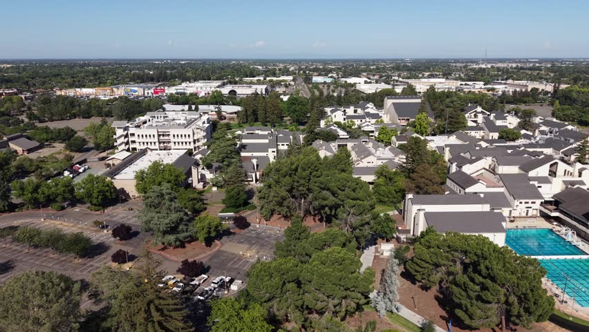 Aerial drone footage flying over the San Joaquin Delta College campus, showing the swimming pool, buildings, and surrounding landscape in Stockton, California on a sunny day