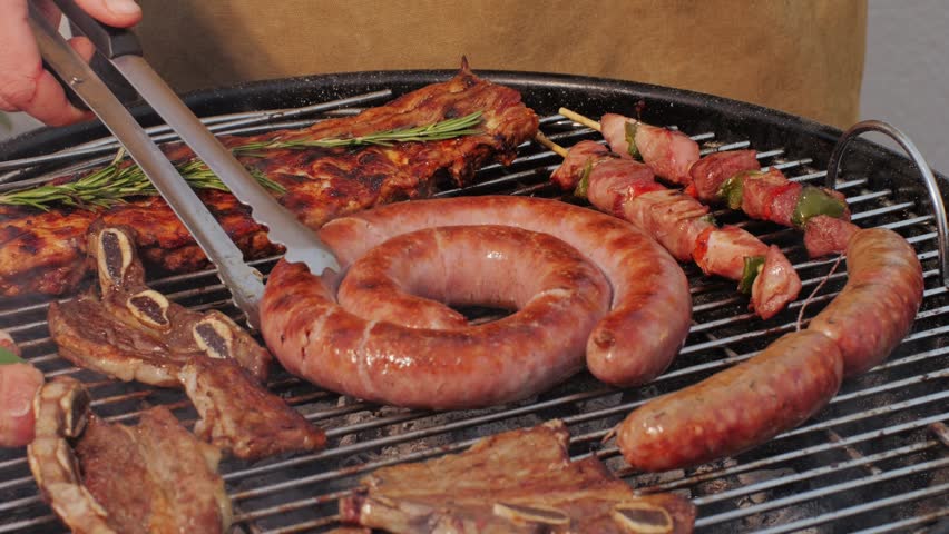 Traditional spanish barbeque, big sausage chorizo botifarra, pork and beef ribs on grill with fire, american style cooking, chef grilling meat fat food, steaks and sausages on bbq.