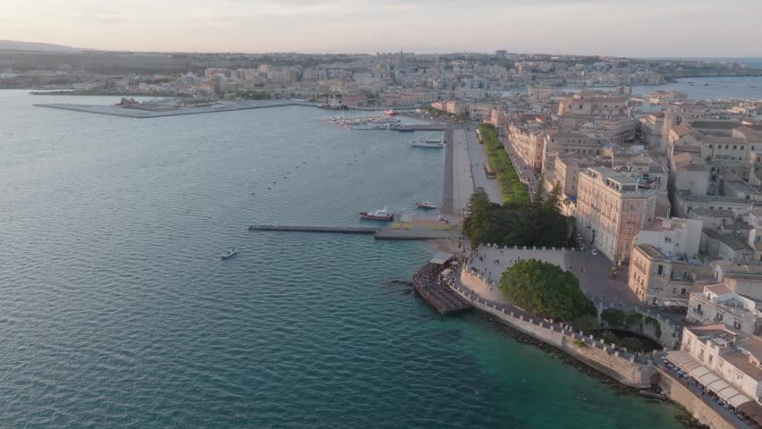 Aerial view of the Island of Ortigia waterfront with historic buildings and calm sea during sunset in Syracuse, Sicily, Italy.