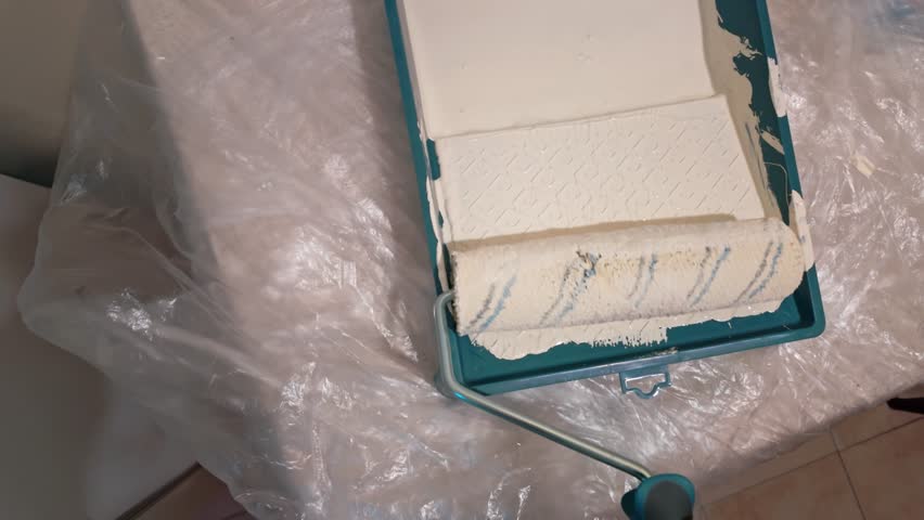 Paint roller loading white paint in tray on covered table.