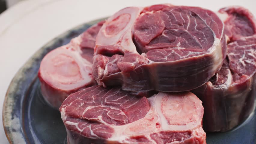 Fresh beef ossobuco steak with salt, spices and herbs on textured background, bones. 