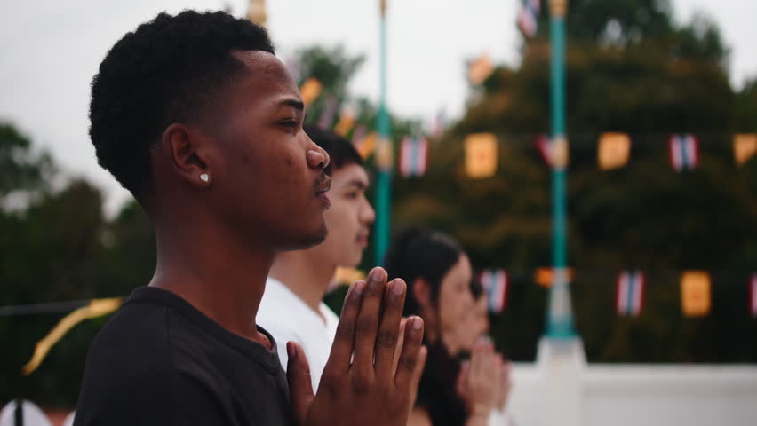 Diverse friends praying together at buddhist temple in thailand