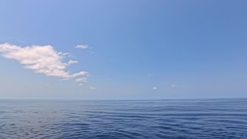At Sea - Seascape view, showing the ocean surface with waves, blue sky and scattered clouds.