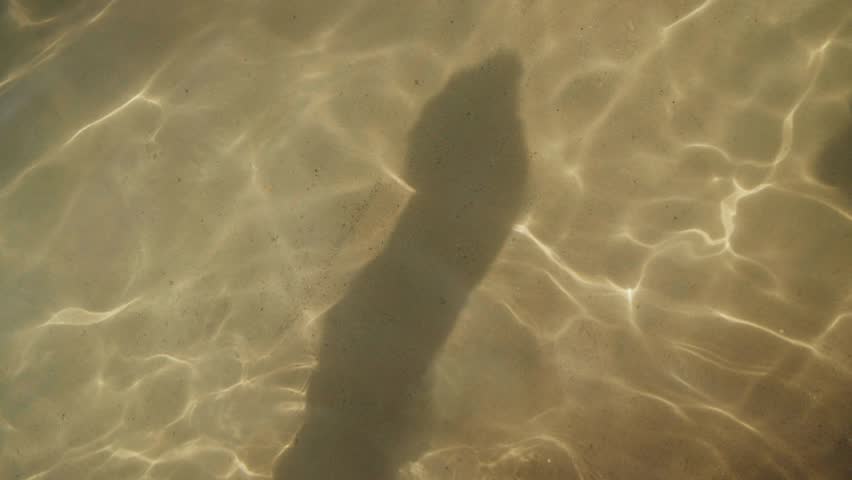 Human shadow silhouette dancing on the sandy sea bottom
