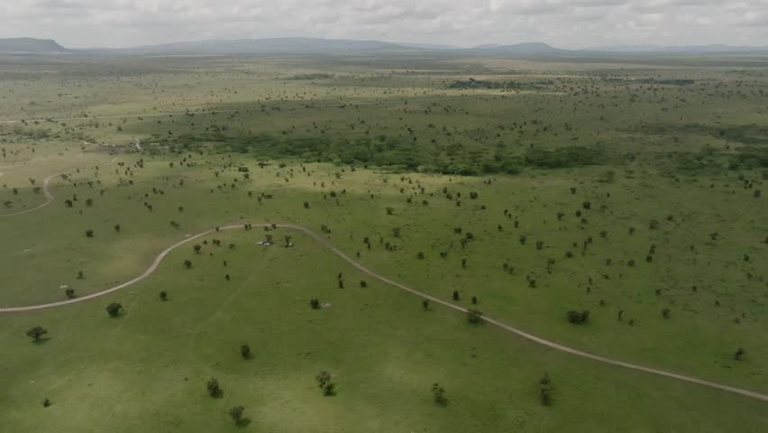 Aerial view of Swara Plains Conservancy with a winding dirt road and scattered trees across the vast savanna under a cloudy sky in Nairobi, Machakos County, Kenya.