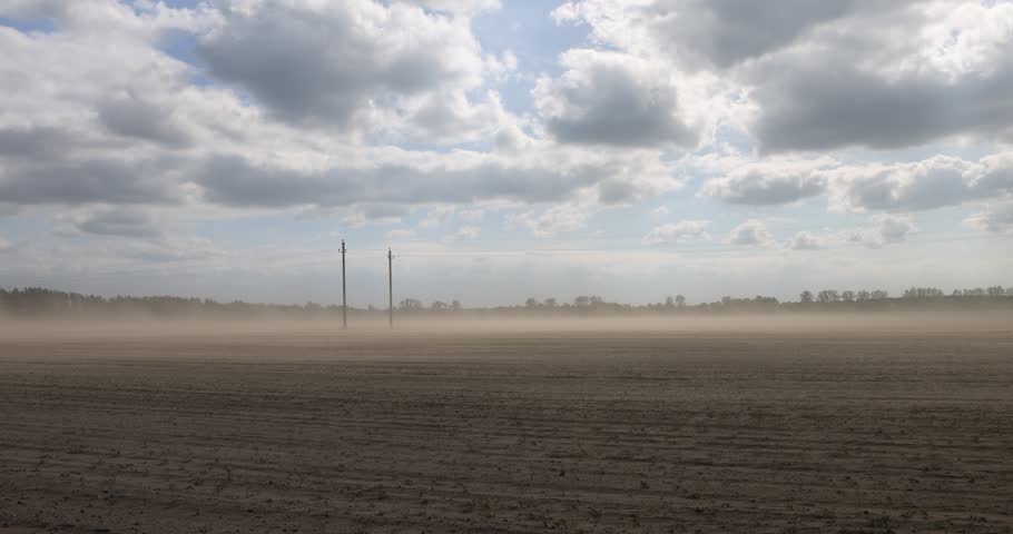 dust storm in windy weather in the field after plowing and preparing the field for sowing, flying dust from strong winds in the agricultural field in the spring season, blue sky with clouds