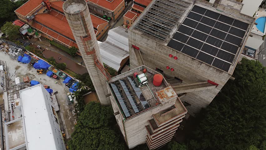Aerial view of SESC Pompéia cultural center by Lina Bo Bardi and surrounding city in São Paulo, Brazil. Orbit and tilt up camera movement.