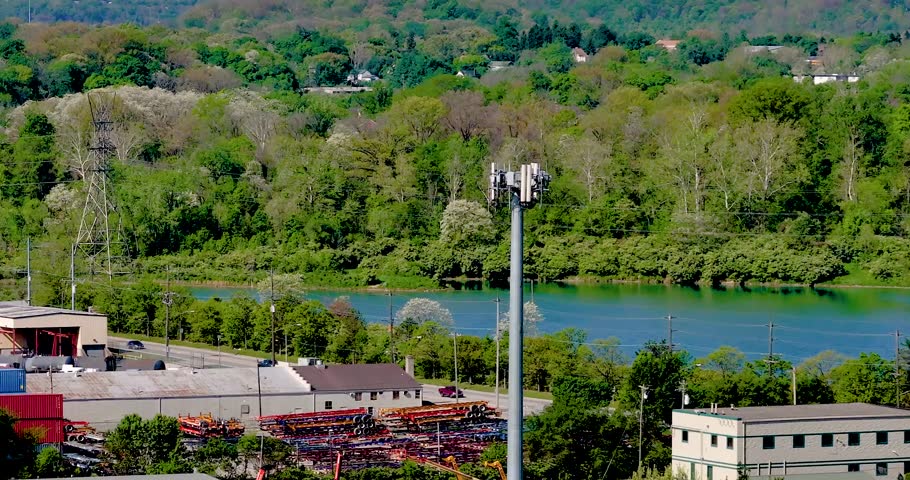 Aerial view of a telecommunications tower standing above industrial buildings and a river with lush green hills in the background in Cincinnati, Ohio, United States.