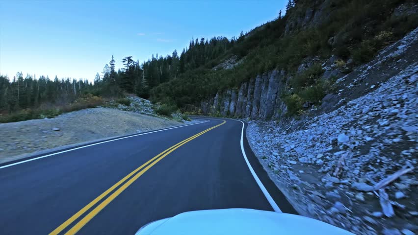 Point of view footage from a vehicle driving along a scenic, winding mountain road near Reflection Lake in Mount Rainier National Park, Washington State, USA. The road is surrounded by dense evergreen