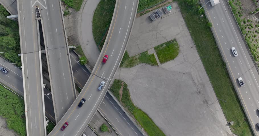 Aerial view of a complex highway interchange with cars driving on multi-level overpasses surrounded by green trees and industrial lots in Cincinnati, Ohio, United States.