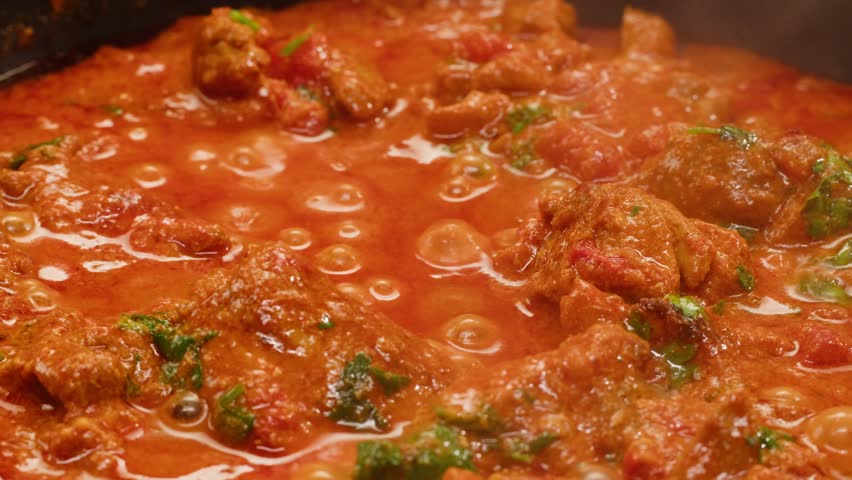 Cooking chicken Indian curry, tikka masala, chicken, lamb, mutton Rogan Josh grill boiling on pan, sauce. Dark background. Close up.