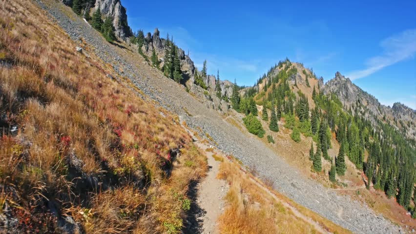 Footage of a picturesque alpine hiking trail, leading through dry grass and rocky slopes towards Sheep Lake and Sourdough Gap in Mount Rainier National Park.
