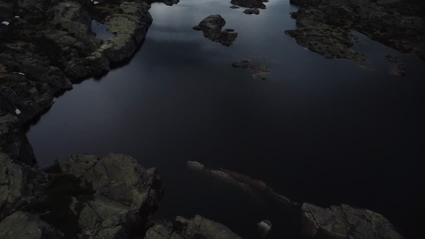 Awe inspiring aerial perspective of a serene, dark mountain lake. The still water reflects the dramatic, cloudy sky and rugged shores