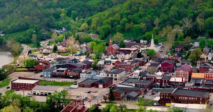 Aerial view of historic downtown buildings and church steeples nestled against lush green hills in Aurora, Indiana, United States.