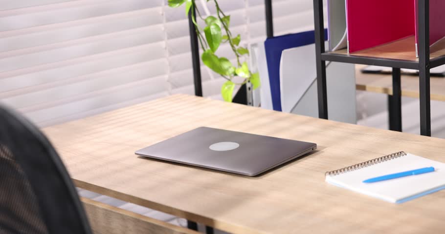 Interior design. Wooden desks with laptops, stationery and shelving unit in office, closeup. Camera moving right