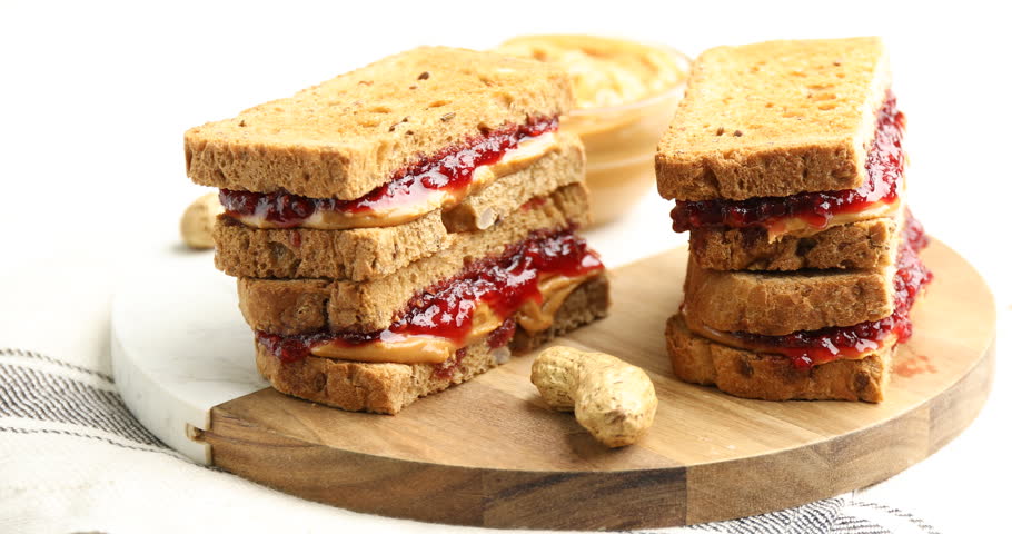 Tasty peanut butter and jelly sandwiches on white table, spinning
