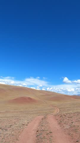 Vertical video of a car driving along a country road under blue sky. Altai desert and semi-desert environment.