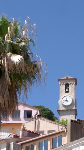Static shot of a stone clock tower above traditional buildings under a clear blue sky