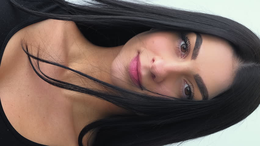 Vertical video. Natural model. Young glamour portrait. Female with long hair casually standing on wind. Attractive chic healthy face skin.
