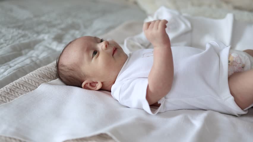 Happy family at home. Mother playing with little toddler child on bed. Mom baby relax playing having fun together. Mother looks at baby with love care. Mom of breast feeding baby rest on bed.