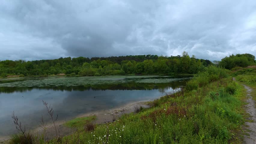 Tranquil lake surrounded by lush green forest under a dramatic, cloudy sky