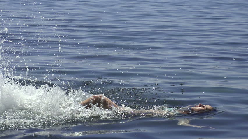 Girl is swimming in the sea on a sunny summer day and making sparkling splashes