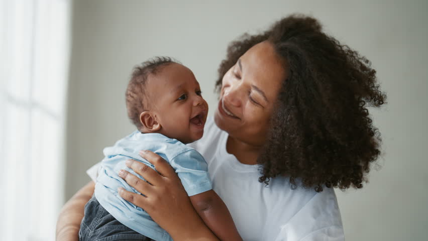 Smiling african infant in mother hands, portrait of mom and baby, happy family. Attractive black woman admiring her pretty little son or daughter, african american ethnicity, love and tenderness