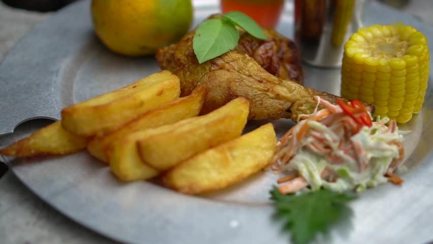 Close up shot of roasted chicken leg served with potato wedges and grilled corn. Delicious grilled chicken platter with crispy french fries and fresh coleslaw salad. Tasty roasted chicken dish garnished with herbs, sweet corn, and thick-cut fries