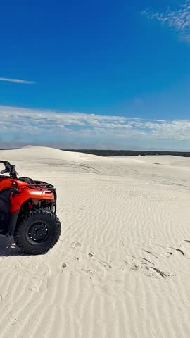 4K video of an Orange quad bike parked on white sand dunes under a blue sky with scattered clouds, creating an adventurous off-road desert landscape scene.