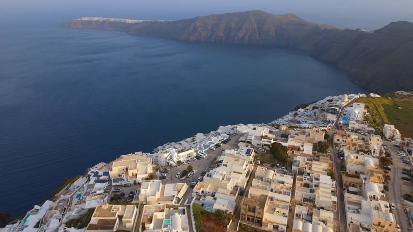 Santorini, Greece. Aplril 18, 2026. Aerial video looking over the whitewashed rooftops and luxury terraces of Imerovigli, Santorini, toward the iconic Oia village and the blue waters of the caldera.