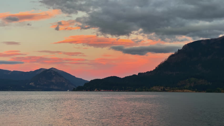Beautiful red and orange sunset sky with large clouds above lake with calm water along mountains with distant peaks