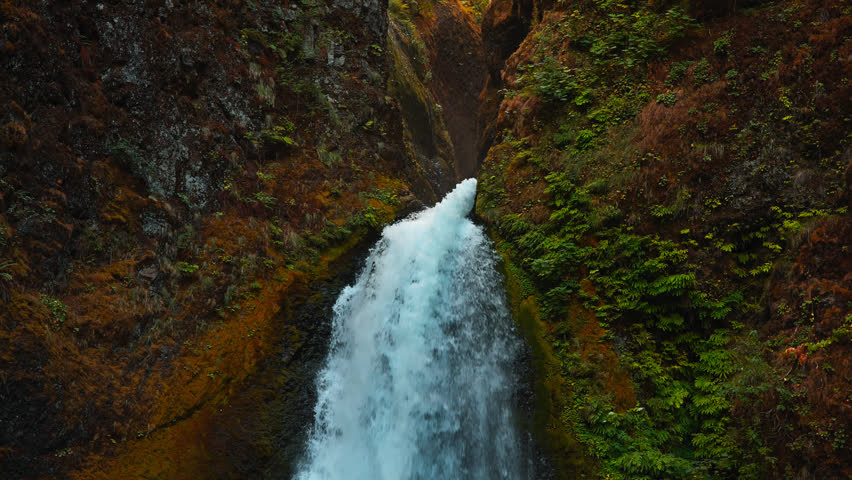 Slow motion closeup of Wahkeena Falls cascading through narrow rocky canyon with moss and greenery tilting down