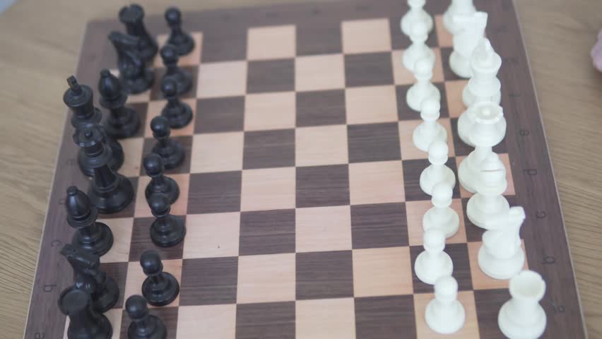 Close-up of a child playing chess alone, moving a piece on a wooden chessboard. Cropped top view showing chess pieces and a hand during a strategy game, with a calm educational and intellectual home