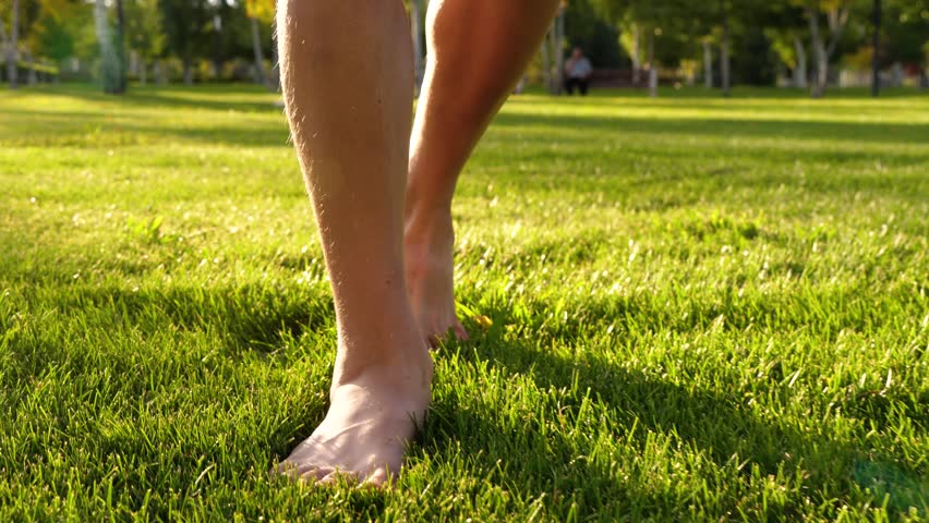 Barefoot walking on fresh green grass in sunny park. Person enjoys nature and tranquility. Relaxing outdoor experience brings peace and joy.