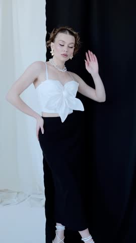 Professional female model wearing white top and black skirt, posing dynamically against minimalist black white background, emphasizing modern fashion styling and versatile wardrobe design