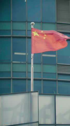 Flag of China waving on a building in Shanghai during the day with clear blue sky and modern architecture visible in the background
