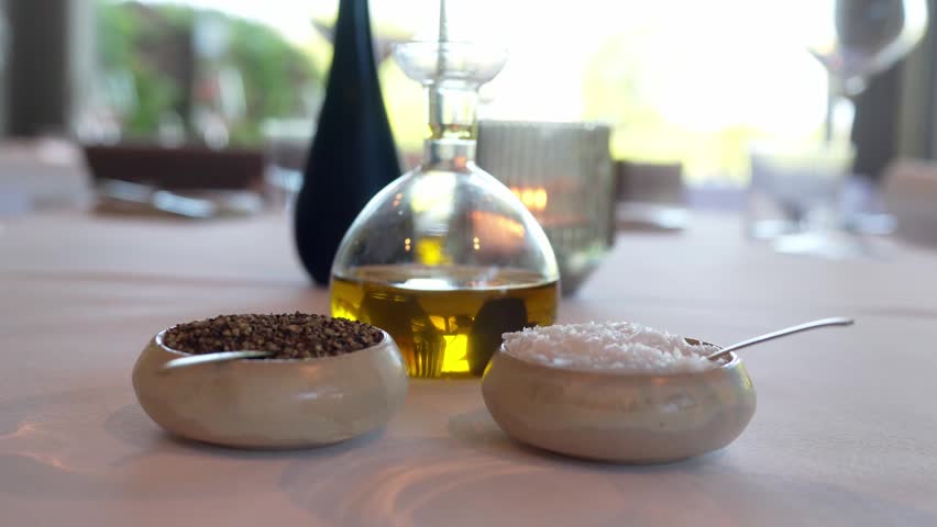 Salt and Pepper inside beautiful bowls with spoons, olive oil in glass see-through cup on decorated dining table inside a luxurious restaurant.