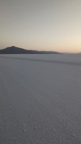 Beautiful sunset over Salar de Uyuni salt flat in Bolivia, scenic wide landscape of white salt desert crust with mountains silhouette at horizon during golden hour dusk in South America