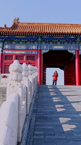 Woman in a red coat standing at a traditional gate in the Forbidden City in Beijing, China, enjoying the sunny day while exploring the ancient imperial palace and its architecture