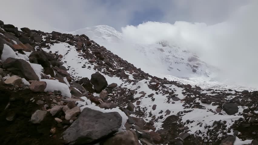 A rugged mountain landscape covered in snow and rocks, with clouds obscuring the summit, evoking a sense of adventure and the wild