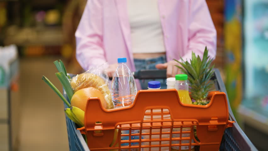 Woman pushing shopping cart full of groceries in supermarket