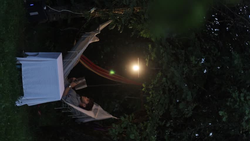 A man lies on a hammock and reads a book in nature
