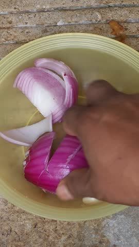 Hand arranging fresh red onion slices and garlic cloves on a plate