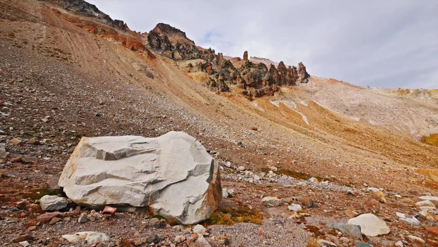 Footage of a large boulder in the foreground with a steep, rocky, and barren mountain slope in the background along the historic Glacier Basin Trail in Mount Rainier National Park, Washington. This mo